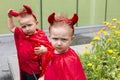 Identical toddler twin disguised as devil scowling with brother in soft focus background