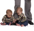 Identical twin baby boys holding dads legs