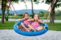 Identical twin girls on spider web nest swing on playground.