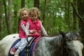 Identical twins enjoying horseback riding in the woods, young pretty girls with blond curly hair on a horse with backlit leaves Royalty Free Stock Photo
