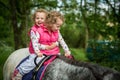 Identical twins enjoying horseback riding in the woods, young pretty girls with blond curly hair on a horse with backlit leaves Royalty Free Stock Photo