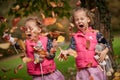 Identical twins having fun with autumn leaves, blond cute curly girls, happy family, beautiful girls in pink jackets