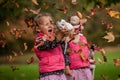 Identical twins having fun with autumn leaves, blond cute curly girls, happy family, beautiful girls in pink jackets