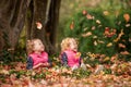 Identical twins having fun with autumn leaves in the park, blond cute curly girls, happy kids, beautiful girls in pink jackets