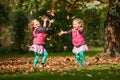 Identical twins having fun with autumn leaves in the park, blond cute curly girls, happy kids, beautiful girls in pink jackets Royalty Free Stock Photo