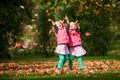 Identical twins having fun with autumn leaves in the park, blond cute curly girls, happy kids, beautiful girls in pink jackets Royalty Free Stock Photo