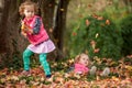 Identical twins having fun with autumn leaves in the park, blond cute curly girls, happy kids, beautiful girls in pink jackets Royalty Free Stock Photo