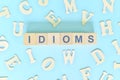 Idioms or idiom concept in English grammar class lesson. Wooden blocks typography flat lay in blue background.