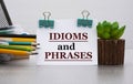 IDIOMS and PHRASES - words on a white sheet with clamps against the background of a cactus and jars with pencils