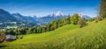 Idyllic alpine landscape with green meadows, farmhouses and snow-capped mountain tops