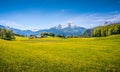 Idyllic alpine landscape with green meadows, farmhouses and snow-capped mountain tops