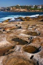 Idyllic and amazing seaside landscape of jagged coast with rocks and water puddles in Clovelly, Sydney. Town on shore across.