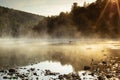 Idyllic bright morning summer sunrise landscape with golden fog on river with haze and sun ripple on water, dark silhouette forest Royalty Free Stock Photo