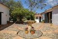 Idyllic cobbled courtyard with a fountain and traditional white building, and trees in background, Villa de Leyva, Colombia