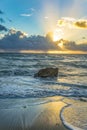 Idyllic colorful ocean sunrise with big waves and boulder