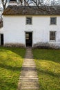 Idyllic path leads through grass to open door of whitewashed stone cottage Royalty Free Stock Photo