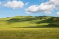 Idyllic scene of green grassy hills dotted with light and shadow from fluffy white clouds in a beautiful blue sky Royalty Free Stock Photo