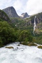 Idyllic scene of a waterfall cascading between mountains and a lush forest on a cloudy day in Norway Royalty Free Stock Photo