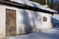 Idyllic Tyrolean mountain hut with a snow-covered roof, wooden door and red-framed window with green shutters. Snow around it Royalty Free Stock Photo