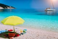 Idyllic white beach with umbrella on lazy summer day. Sailing boat at anchor in calm crystal clear blue sea water