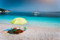 Idyllic white beach with umbrella on lazy summer day. Sailing boat at anchor in calm crystal clear blue sea water