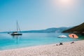 Idyllic white beach with umbrellas on lazy summer day. Sailing boat on calm crystal clear water