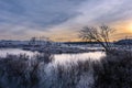Idyllic winter scene with a river partially frozen over and illuminated by a setting sun. Royalty Free Stock Photo