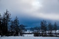 Trees and mountains shrouded in fog, dark clouds. Snow-covered landscape