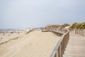 View of pedestrian wooden path on beach, people walking and people taking sunbath on beach, lighthouse as background