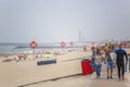 View of pedestrian wooden path on beach, people walking and people taking sunbath on beach, lighthouse as background