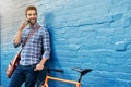 Ill be rolling your way soon. a handsome young man leaning against a wall with his bike talking on a cellphone. Royalty Free Stock Photo