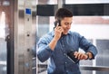 Ill be there shortly. a young businessman talking on a cellphone and checking his watch while standing in an elevator. Royalty Free Stock Photo