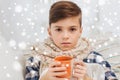 Ill boy with flu in scarf drinking tea at home Royalty Free Stock Photo