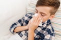 Ill boy lying in bed and blowing his nose at home Royalty Free Stock Photo