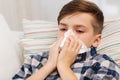 Ill boy lying in bed and blowing his nose at home Royalty Free Stock Photo