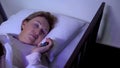 Ill female sleeping in sickbed in hospital, holding remote control, TV lights