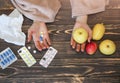 Ill girl with a flu is sitting at the wooden table with pills and fruit. Woman with cold is holding medicine and apples in hands.