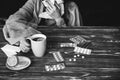 Ill girl with a flu is sitting at the wooden table with pills and tea. Woman sneezing. Runny nose and cold. Weak immunity. Winter