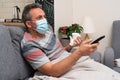 Ill male model wearing medical mask zapping tv holding tissue