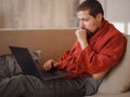 Ill man covered in warm blanket looking at laptop screen