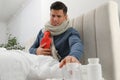 Ill man with hot water bottle taking pills from bedside table at home Royalty Free Stock Photo