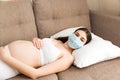 Ill pregnant woman in protective medical mask is falling asleep on the sofa at home. epidemic concept. Respiratory