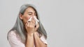 Ill senior woman with cold blowing nose in napkin