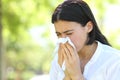 Ill woman sneezing covering mouth with a wipe in a park