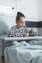 Ill young patient playing on smartphone while resting on bed in pediatric hospital room. Royalty Free Stock Photo