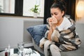 Ill young woman sit on sofa covered with blanket, freezing, blowing her runny nose, sneeze in tissue. Female got fever Royalty Free Stock Photo