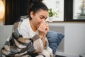 Ill young woman sit on sofa covered with blanket, freezing, blowing her runny nose, sneeze in tissue. Female got fever Royalty Free Stock Photo