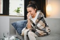 Ill young woman sit on sofa covered with blanket, freezing, blowing her runny nose, sneeze in tissue. Female got fever Royalty Free Stock Photo