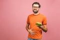 Illness sad young man in casual put hand on pain abdomen, stomach-ache, standing and holding burger isolated on pinke background. Royalty Free Stock Photo