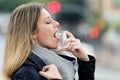 Illness young woman applying a analgesic spray to soften the throat in the street. Royalty Free Stock Photo
